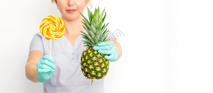 菠萝棒棒糖年轻caucasian女医生营养学家 手持新鲜菠萝和棒棒糖的白色背景护理治疗横幅生态微笑饮食热带女性卫生外套背景