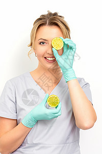 橙片女人年轻微笑的女性美容师用石灰片遮住眼睛的肖像 在白色背景上戴手套嘴唇女孩隐藏卫生医生橙子身体保健皮肤护理背景