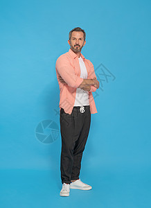 时髦的中年灰发男子双臂交叉 穿着粉红色衬衫和黑色慢跑裤 与黄色背景隔离 看着镜头 成熟适合的人 健康生活方式概念背景图片