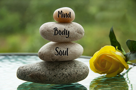 身体心灵灵魂雕刻在具有模糊性和黄色玫瑰背景的zen石块上的心灵 身体和灵魂等字眼 复制空间和Zen概念背景