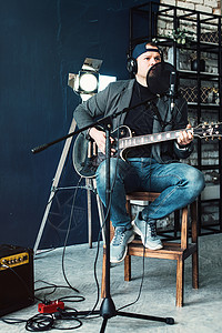 唯一性一个男歌手坐在一个椅子上 耳机里坐着一小凳子 吉他在家庭工作室录音扬声器居住嗓音流行音乐唱歌演员男性人声记录麦克风背景