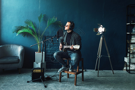 男歌手坐在凳子上 戴着耳机 吉他在家庭录音室录制曲目记录人声唱歌创新生产麦克风收音机歌曲广播唯一性背景