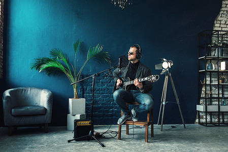 唯一性男歌手坐在凳子上 戴着耳机 吉他在家庭录音室录制曲目生产流行音乐卡拉ok电缆创造力嗓音独创性工作室扬声器记录背景