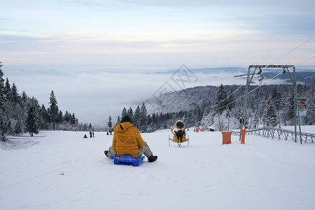 在德国黑森州 Ren 的山上 一名男子在壮丽的冬季景观背景下骑着雪橇 神奇的高大苍松和雪杉覆盖着冰雪 地平线创造了一种幻觉 并与背景