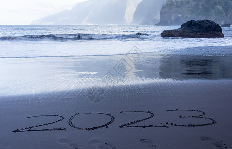 写在黑沙沙滩上的2023年符号旅游海洋异国情调新年海浪海滩假期旅行日历背景图片