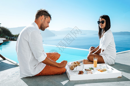 游泳周年店庆在希腊度假的情侣男人和女人在游泳池吃早餐新郎酒店女性奢华巡航拥抱丈夫泳池周年友谊背景