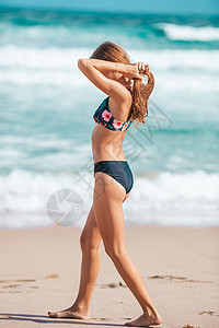 泳装步行穿着泳衣的可爱瘦瘦女孩 在海滩上有一个完美的身材热带海岸海浪游泳身体童年旅游支撑情调海洋背景