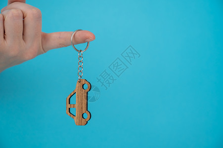 女人的手握着木钥匙链 车形是蓝色背景的汽车生态价格钥匙圈手指车辆礼物女性展示交易商业背景图片