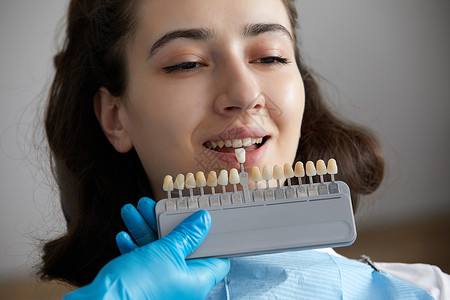 牙医为病人选择牙釉质的颜色 牙医将牙釉质标本应用于白人女性牙齿矫正阴影成人卫生医生药品专家女士工具诊所背景图片
