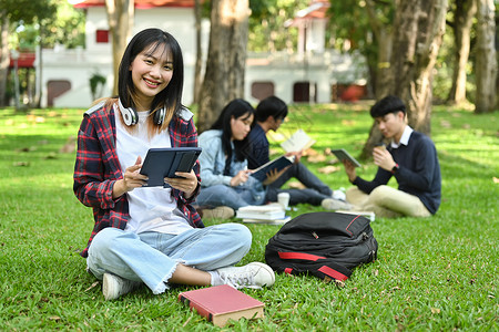 校园四有在校园绿草上使用数字平板电脑的亚洲女子学院或大学女生和大学生 令人欢欣鼓舞背景