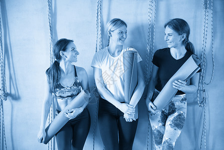 一群穿着运动服的女性朋友在瑜伽锻炼后站在健身房里微笑着 妇女站在墙边 带运动垫蓝色男人护理训练朋友们健康班级工作室女孩们运动背景图片