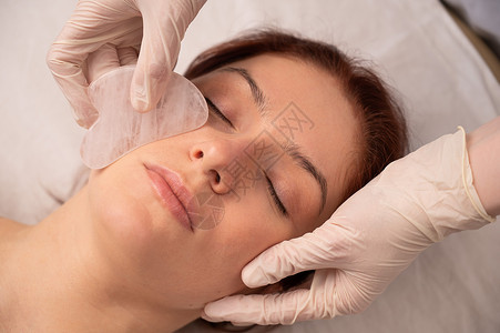 美容师在客户脸上用牙甲擦伤器沙龙石头护理刺激美容女性享受女士病人皮肤图片