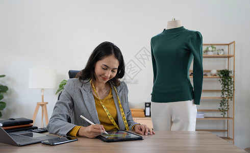 时装素材网站微笑设计师 快乐造型师亚洲年轻女性 使用笔记本电脑在家办公室查看在线订单的女孩 销售时装 创业公司所有者 电子商务企业家 小型中背景