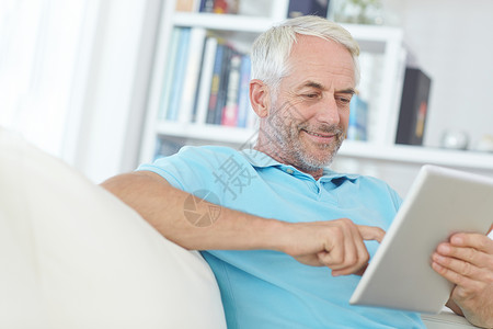 客厅素材网站成熟的男人 数字平板电脑或在家里 家里或公寓客厅的沙发上放松 玩社交媒体应用程序或网络游戏 微笑 快乐或退休的人在技术填字游戏或背景