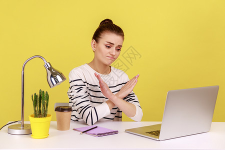 坐在工作场所的妇女交叉手举有X符号 在笔记本电脑屏幕上面露脸图片