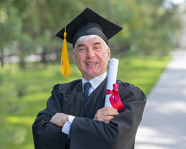 身着毕业礼服 手持文凭的老人在户外露面 (笑声)背景图片