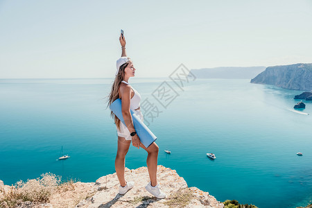 心中有戒在平静的蔚蓝大海上用瑜伽垫的女人 漂亮的中年妇女留着长头发 在海边有蓝色瑜伽垫的健身教练 女性健身瑜伽常规概念 健康的生活方式戒背景
