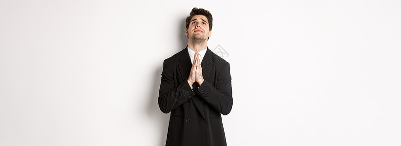 身穿黑西装的有希望又充满麻烦的男人求神 恳求和仰望 需要帮助 站在白背景上站立套装老板企业家办公室工作商业横幅成功广告经理背景