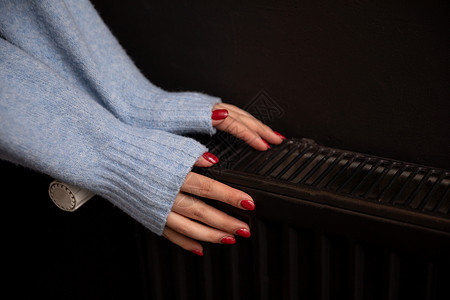 放出女人的冷手放在房间里的热散热器上用户持有暖手热能测量手指季节控制消费者生态背景