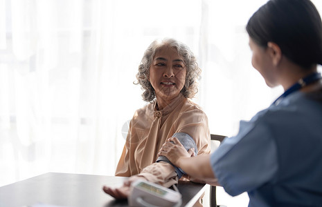 护理员女护士正在为一名老年女性患者测量血压 医生在养老院为一位老年妇女测量血压 女性看护者和老年女性一起在家压力退休女士诊所医疗成人检背景