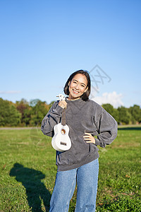 美丽的女孩在阳光明媚的日子里 站在绿地上 穿着柔丽的秋露打扮 展示音乐乐器背景