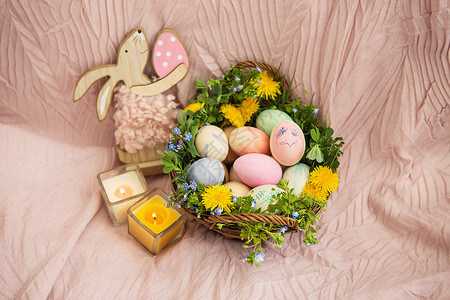 粉色蛋柔和的床罩上放着一篮草和各种鲜艳的花朵 一只兔子 篮子里有复活节彩蛋 彩蛋上绘有美丽柔和的水彩画背景