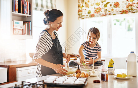 消耗品让她的女儿对烘焙产生热情 一个小女孩和她妈妈在厨房里烤面包背景