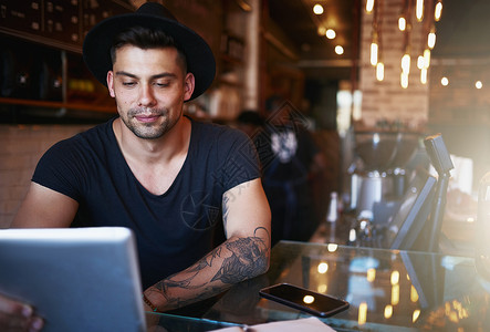 密切关注他的咖啡店的表现 一个在咖啡店工作时使用数字平板电脑的年轻人图片