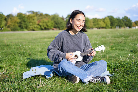 绿色吉他素材棕褐发女孩快乐 学生在公园的草地上玩木偶游戏 放松 歌唱 生活方式概念歌曲音乐家吉他幸福成人乐器弦琴唱歌女性乐趣背景