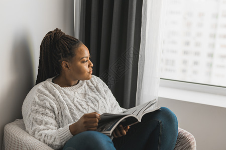八卦杂志留辫子的非洲裔美国女性在家阅读杂志  休闲和生活方式概念报纸卧室情感女孩闲暇快乐八卦微笑文学享受背景