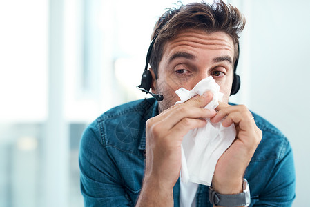 我今天在办公室生病了一整天 一名男性呼叫中心代理在他的办公室用纸巾擤鼻涕背景图片