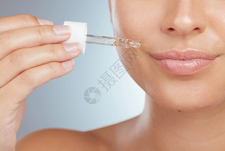 一位不知名女性使用滴管将面部精华素涂抹在嘴唇上的特写镜头 在工作室中灰色背景下隔离的白种人模型在护肤程序中使用皮肤油使皮肤健康发背景图片