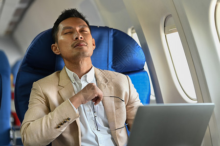 而荒于戏千年商务人士在飞机机舱坐着舒适的座位时 分心于计算机工作而离开电脑工作背景