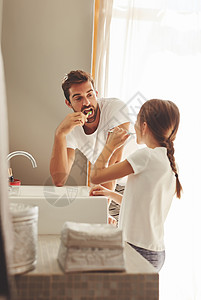 父亲就像大树就像这样……一个英俊的年轻人和他的小女儿在浴室里刷牙背景