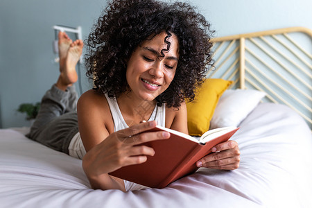 冷静一下快乐的年轻多种族女人躺在床上 在家里看书放松一下 在床上背景