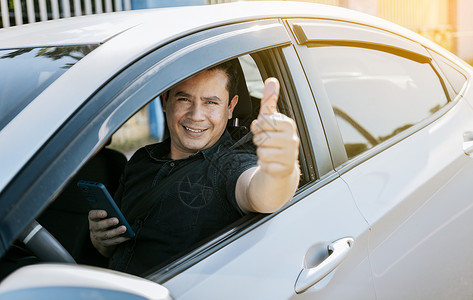 拿着手机的微笑司机竖起大拇指 司机拿着手机竖起大拇指 快乐的司机在路上竖起大拇指 安全驾驶理念背景图片