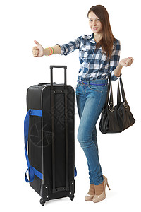 16 岁的女孩穿着牛仔裤和格子衬衫 搭便车或出租车站 16 岁的少女 背着一个带轮子的黑色大旅行包背景图片