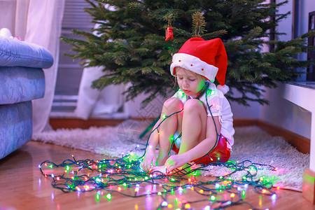 穿着圣诞圣诞老人帽子的小美女孩 坐在圣诞树下 在花冠上 婴儿 微笑图片