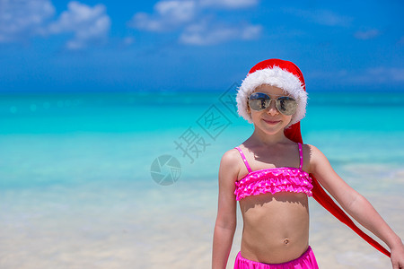 热带海滩上的红色圣诞礼帽的小可爱女孩 快乐的背景图片