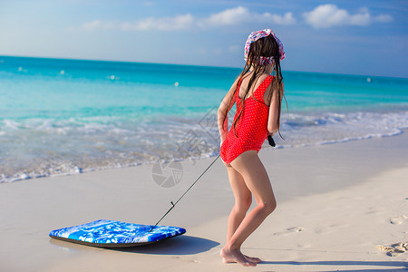 可爱的小可爱女孩在白岸上拉着一个冲浪板 孩子背景图片
