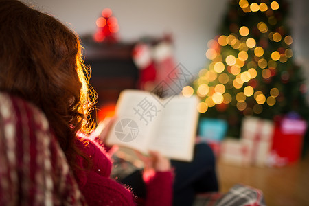 圣诞节红头发阅读的近视 书 小玩意儿 圣诞树 客厅 扶手椅背景图片