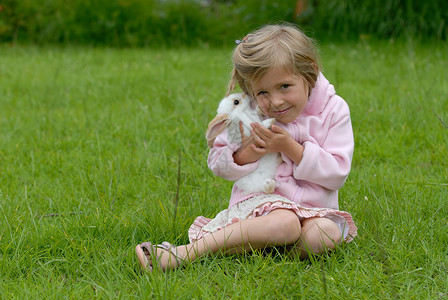 穿粉红色衣服的可爱小女孩在照顾小白兔 复活节兔子图片