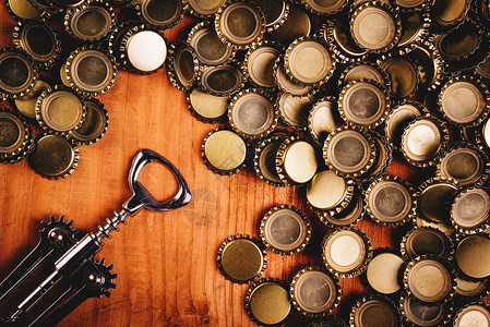 古老的瓶装开瓶器和一堆啤酒瓶盖 木板 酒精 帽子背景图片