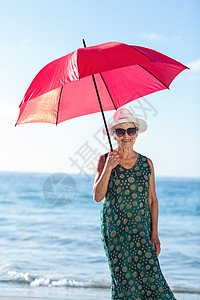 穿着雨伞的年长妇女 海洋 老年 快乐 海滩 假期 红色的背景图片