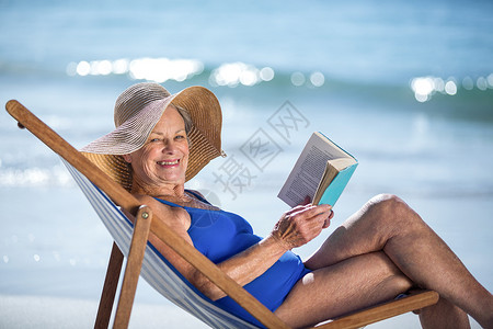 美貌成熟的女人在读一本书 躺在甲板椅子上 水 高级的背景图片