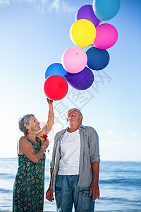 持有气球的老年夫妇 晴天 海洋 男人 波浪 女士 微笑背景图片