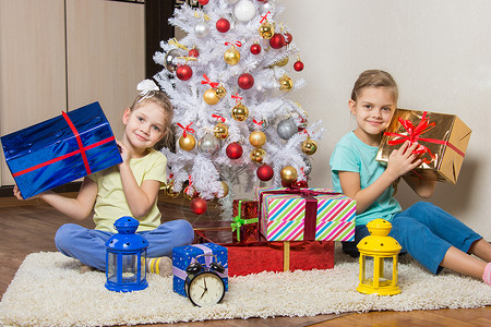 2个小女孩 早上一大早带着圣诞礼物 坐在圣诞树旁边的圣诞树边背景图片