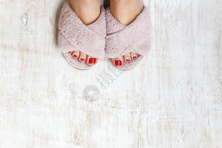 毛毛鞋双脚和红指甲 在家庭毛毛 毛毛的粉红色拖鞋上 衣服 凉鞋背景