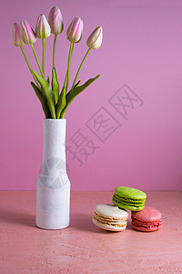 马卡罗恩斯的粉色背景 位于郁金香花瓶旁 祝贺背景图片