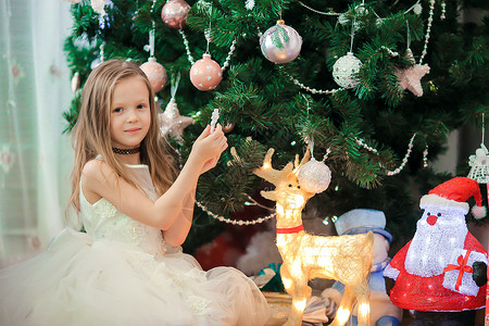 小女孩和鹿在圣诞树附近的可爱的小女孩 圣诞树下的孩子们带着礼品盒 喜悦 惊喜背景